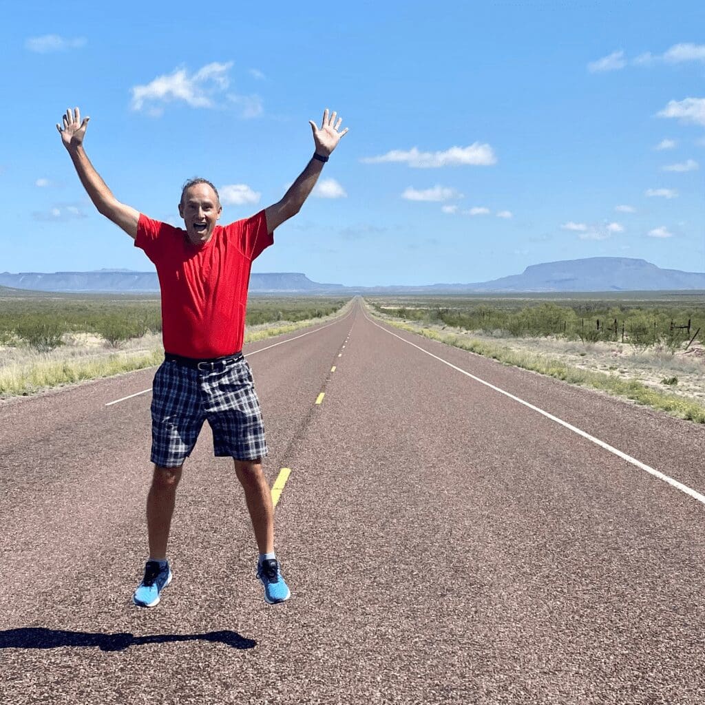 A man jumping on a long section of straight highway with mountains in the background
