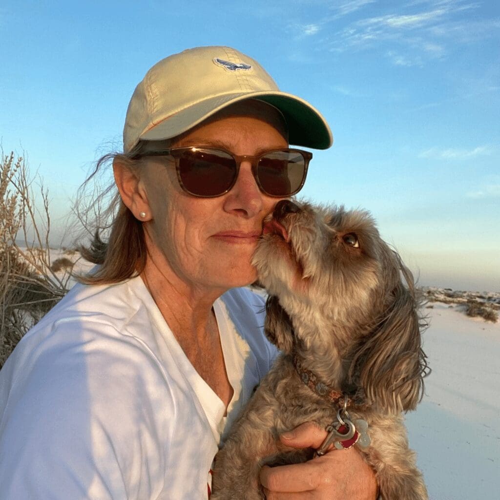 A woman holding gray dog close to her with white sand dunes in background