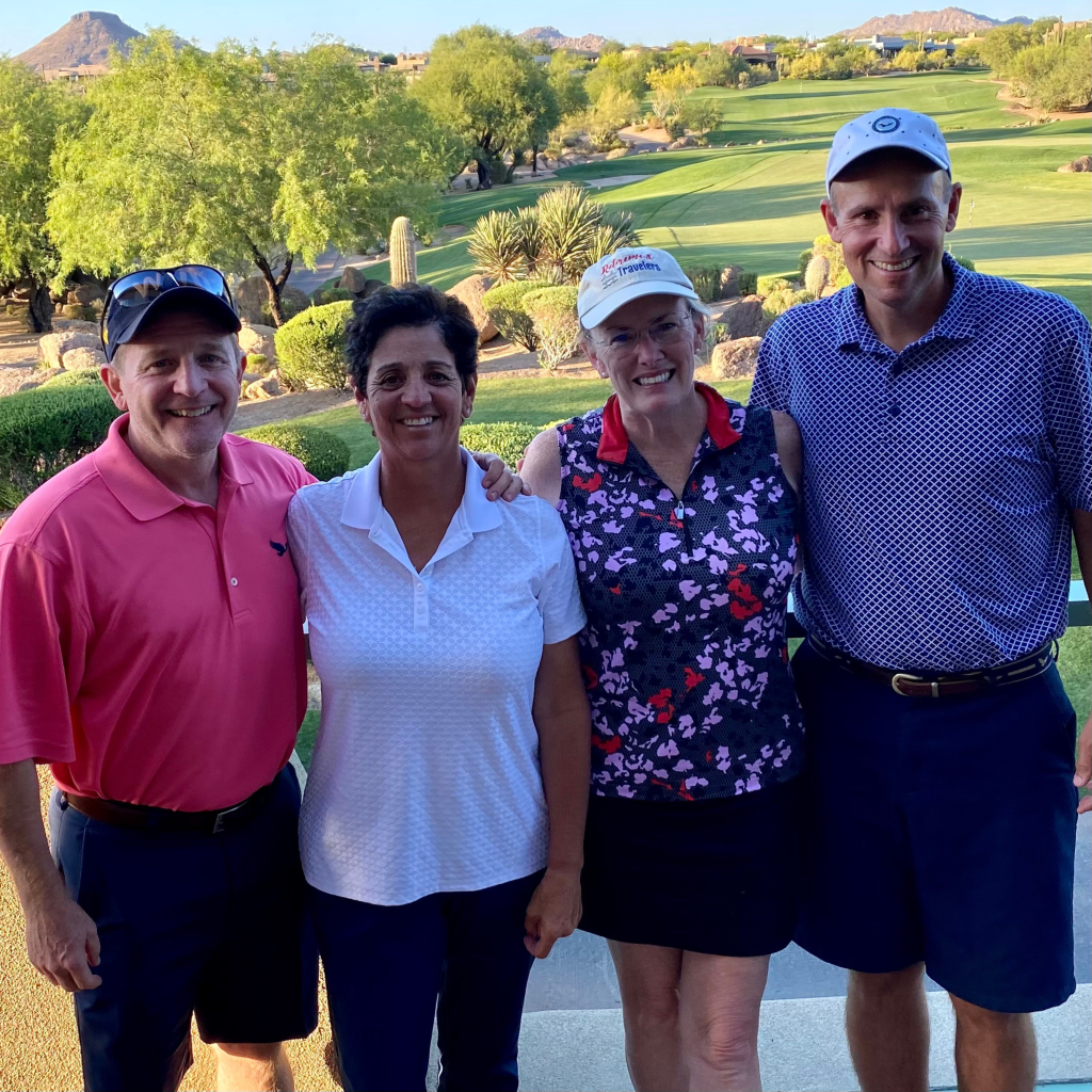 Two couples standing with a golf course in the background