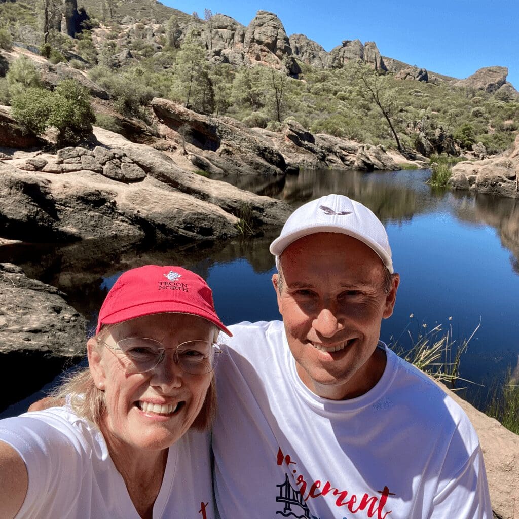 A man and woman standing with a small lake and pinnacle rocks in the background