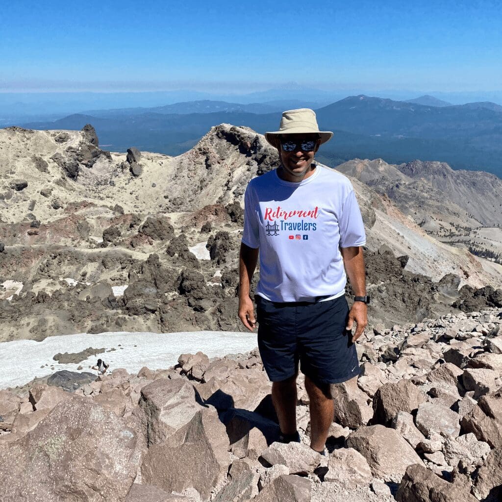 A man standing on top of a tall mountain with other mountains in the background