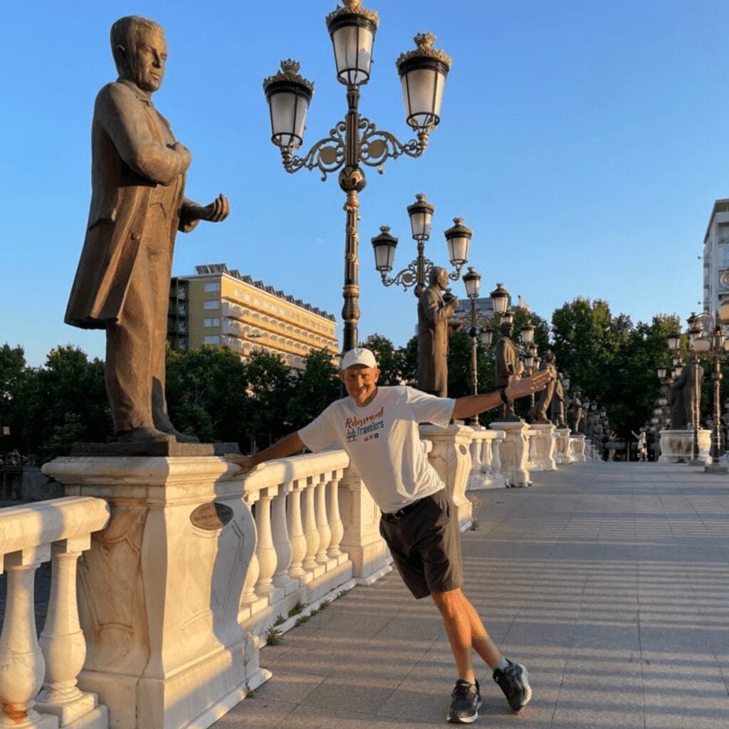 John standing on bridge with statues lining the bridge colomns