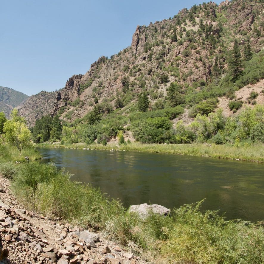a river surrounded by green grass and trees and rocky ledges of hills around