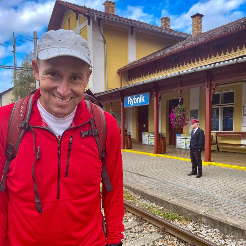 john in foreground with train conductor in uniform in background standing next to Yellow train station