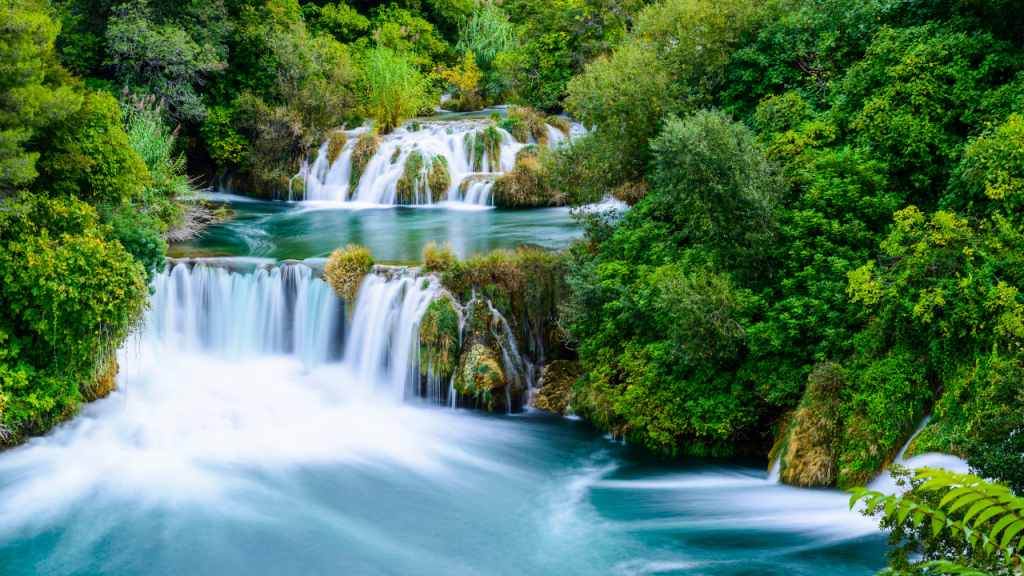 a multi-tiered waterfall with green trees