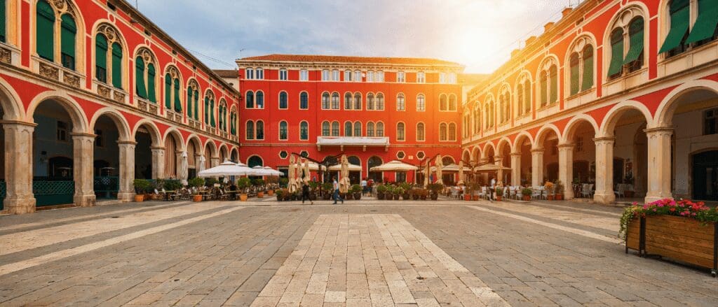 a big square with red building and arches along the sides