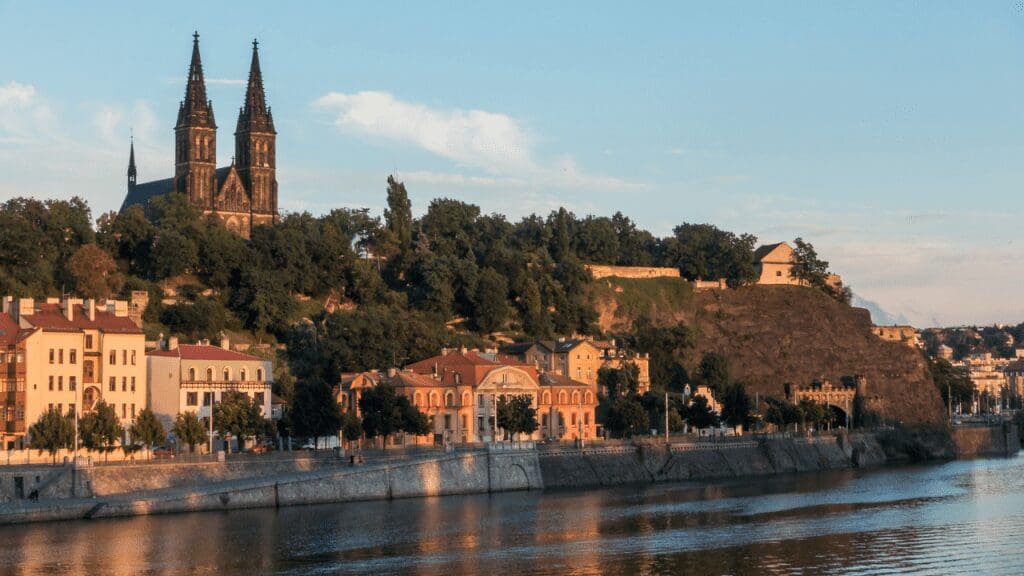 a castle fortress with a two-spire church along the banks of the river in Prague