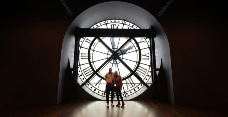 Man and woman standing in front of large clock in the Musee D’Orsay in Paris, France