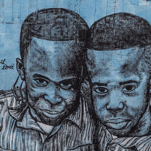 Street art in Medellin colombia of 2 small boys with birds on their shoulders with an overall blue tint