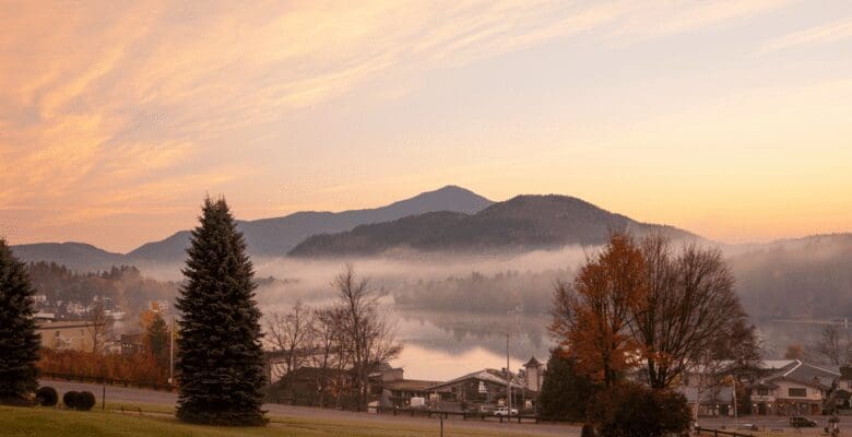 Morning view of fog over Lake Placid with mountains in the background and a cottage in the foreground