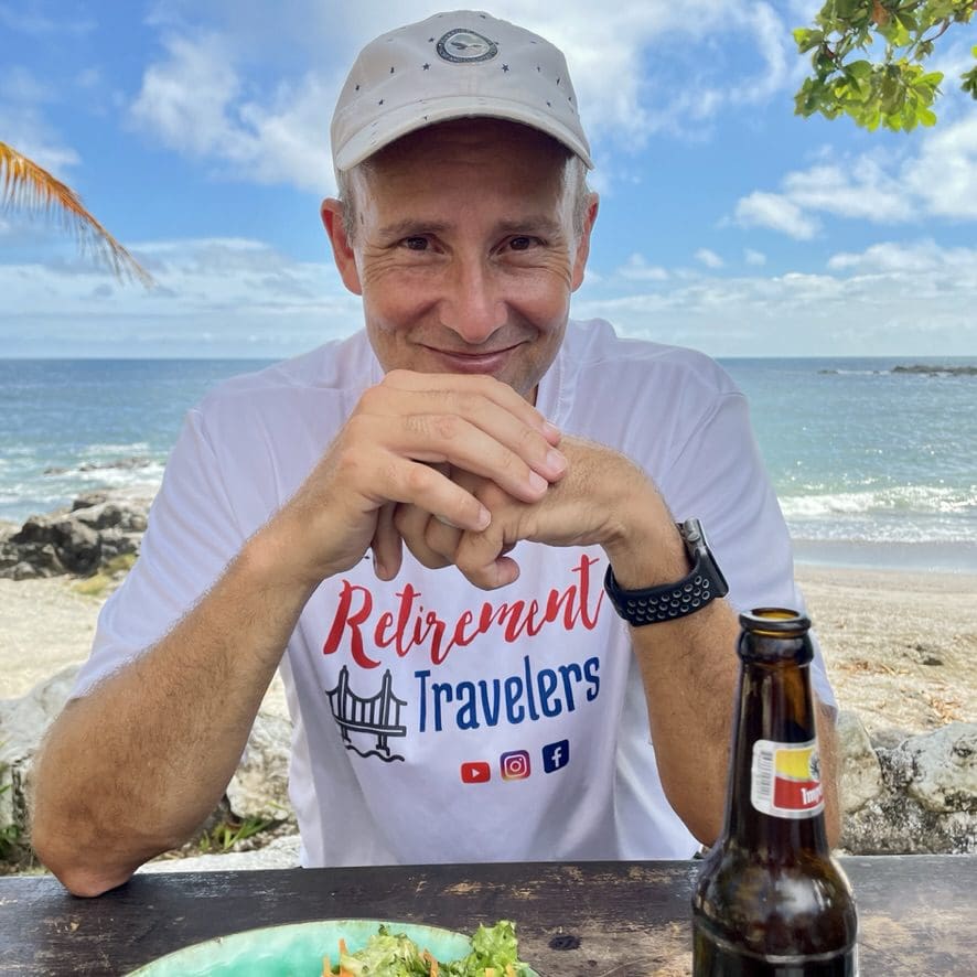 man sitting at a table with a beer and ocean in background