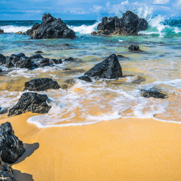 Ocean Waves crashing against black lava rocks with yellow sand in Maui, Hawaii