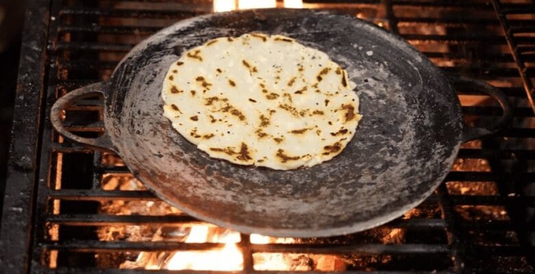 Corn tortilla in a metal skillet over open flames on a grill