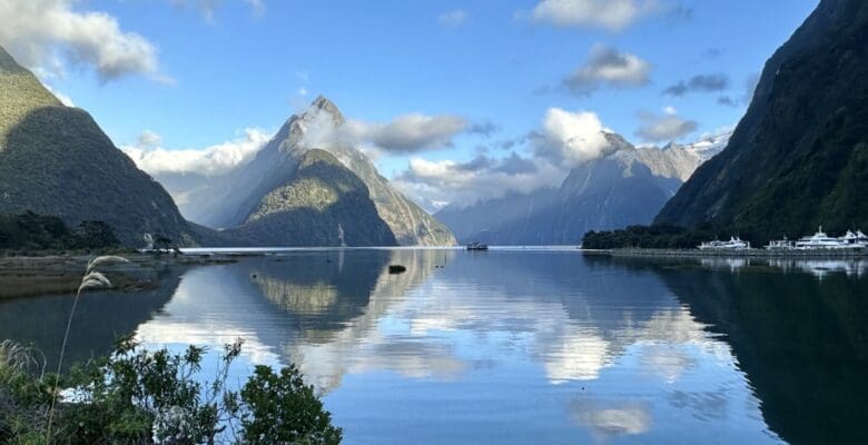 Beautiful still body of water surrounded by steep, large mountains reflecting in the water.