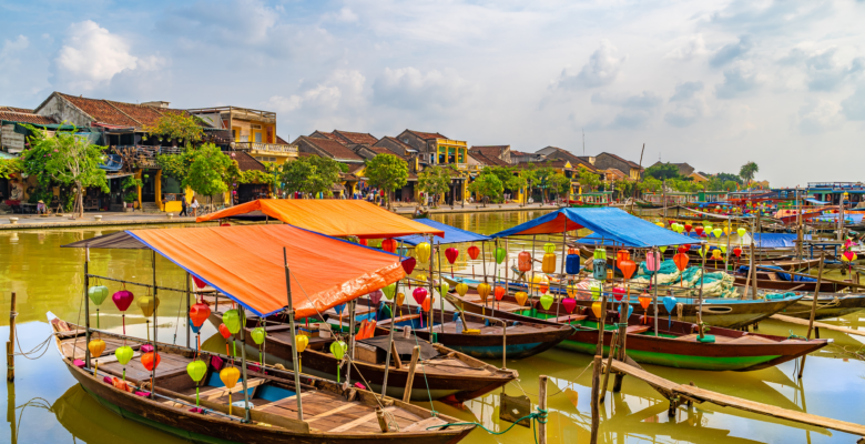Wooden boats with colorful lanterns docked in water along the city of Hoi An.